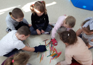 Dzieci w grubych rękawicach przekładają do siebie kolorowe patyczki